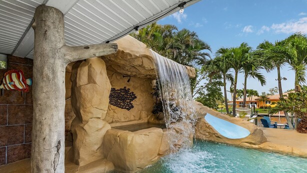Ein Poolbereich mit Wasserfall, Palmen und einer überdachten Sitzgelegenheit.