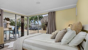 Ein Schlafzimmer mit einem großen Bett, Blick auf den Strand und einer Essecke mit Außenbestuhlung.