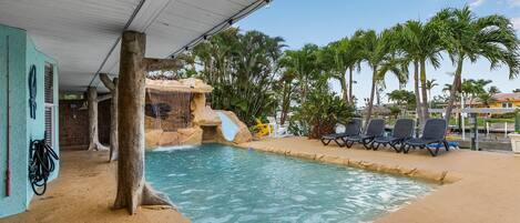 A pool area with a waterfall feature, lounge chairs, and palm trees.
