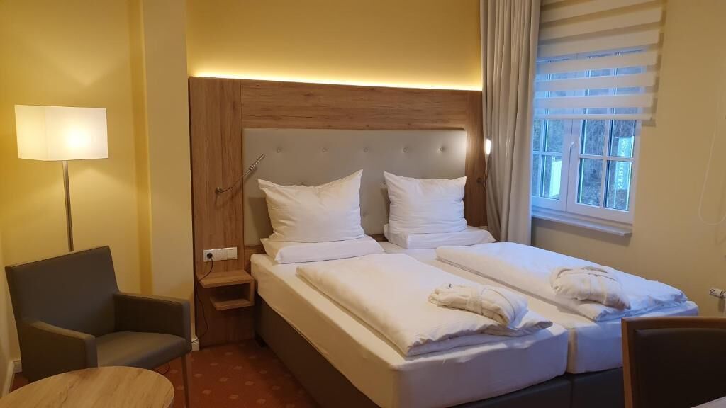 Ein Hotelzimmer mit Doppelbett, Nachttisch, Lampe, Stuhl und einem Fenster mit Jalousien.