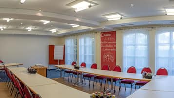 Un salón de conferencias con una larga mesa, sillas rojas, una pizarra y un cartel con texto.
