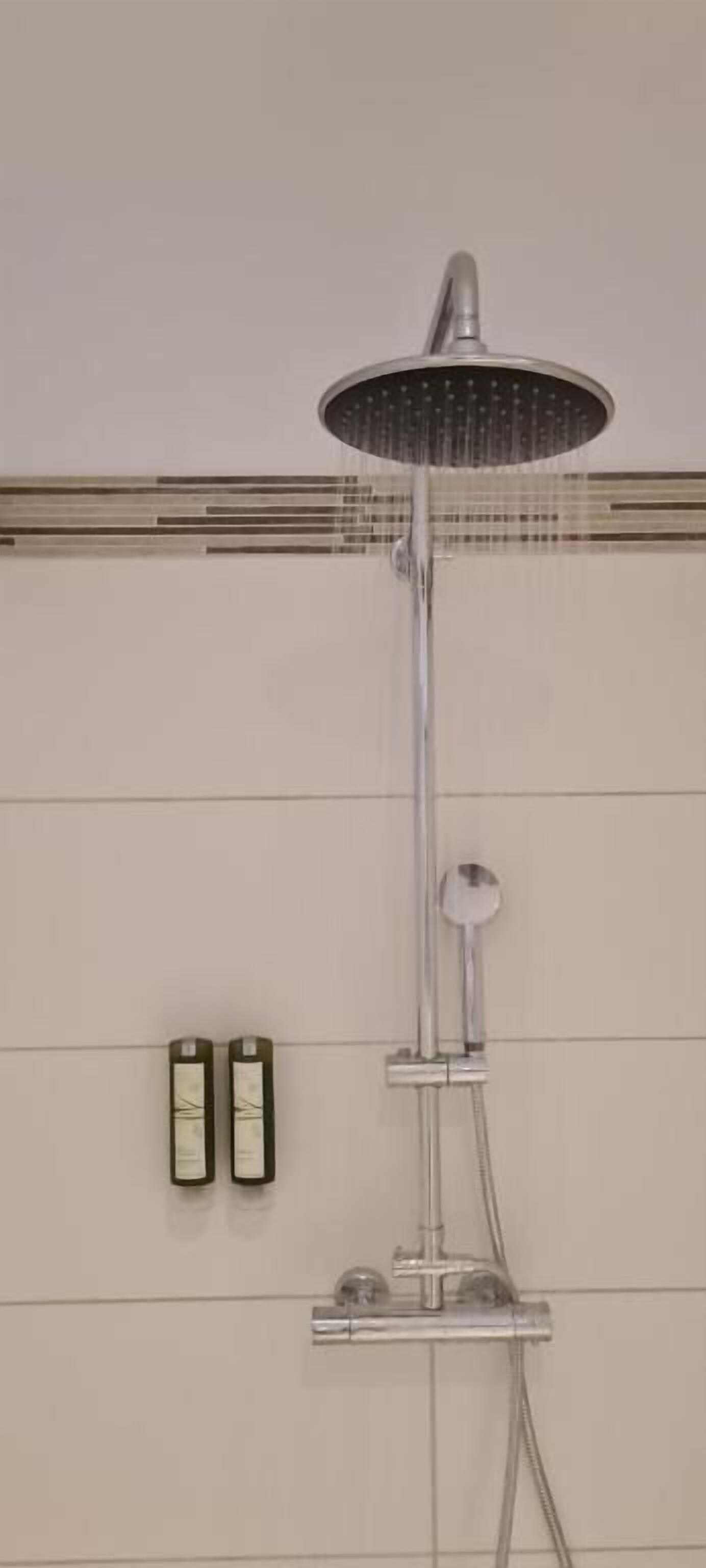Une pomme de douche avec un effet de pluie, un flexible de douche et un panneau de commande fixé au mur.