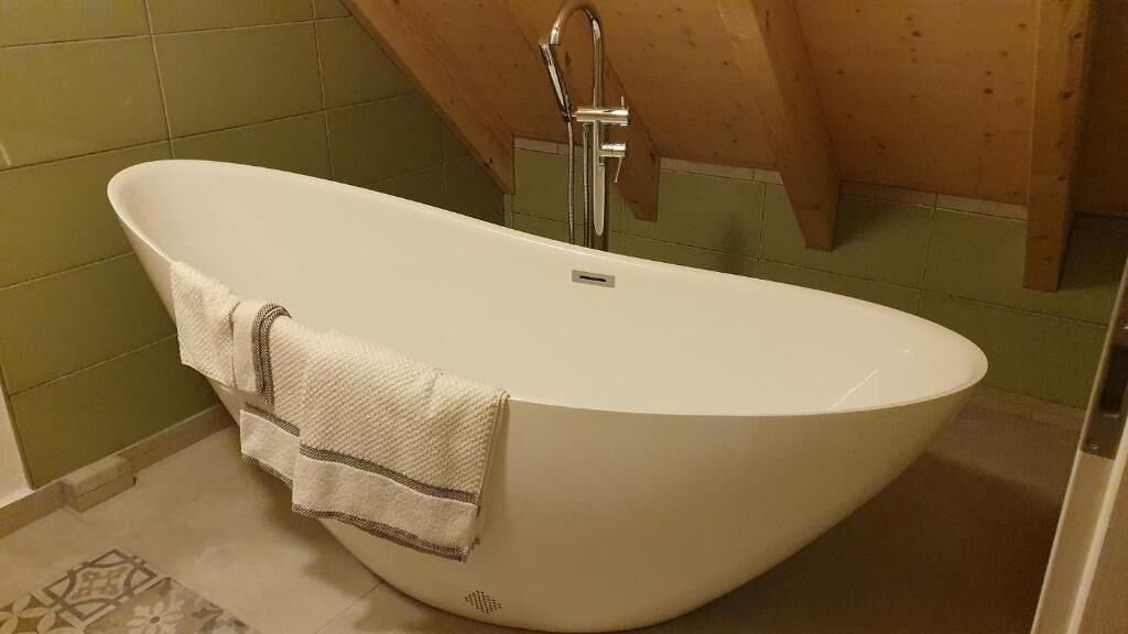 Una bañera independiente en un baño con azulejos verdes y techo de madera.