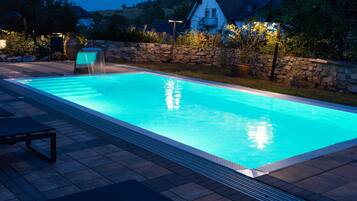 A rectangular swimming pool with a stone wall and a clock in the background.