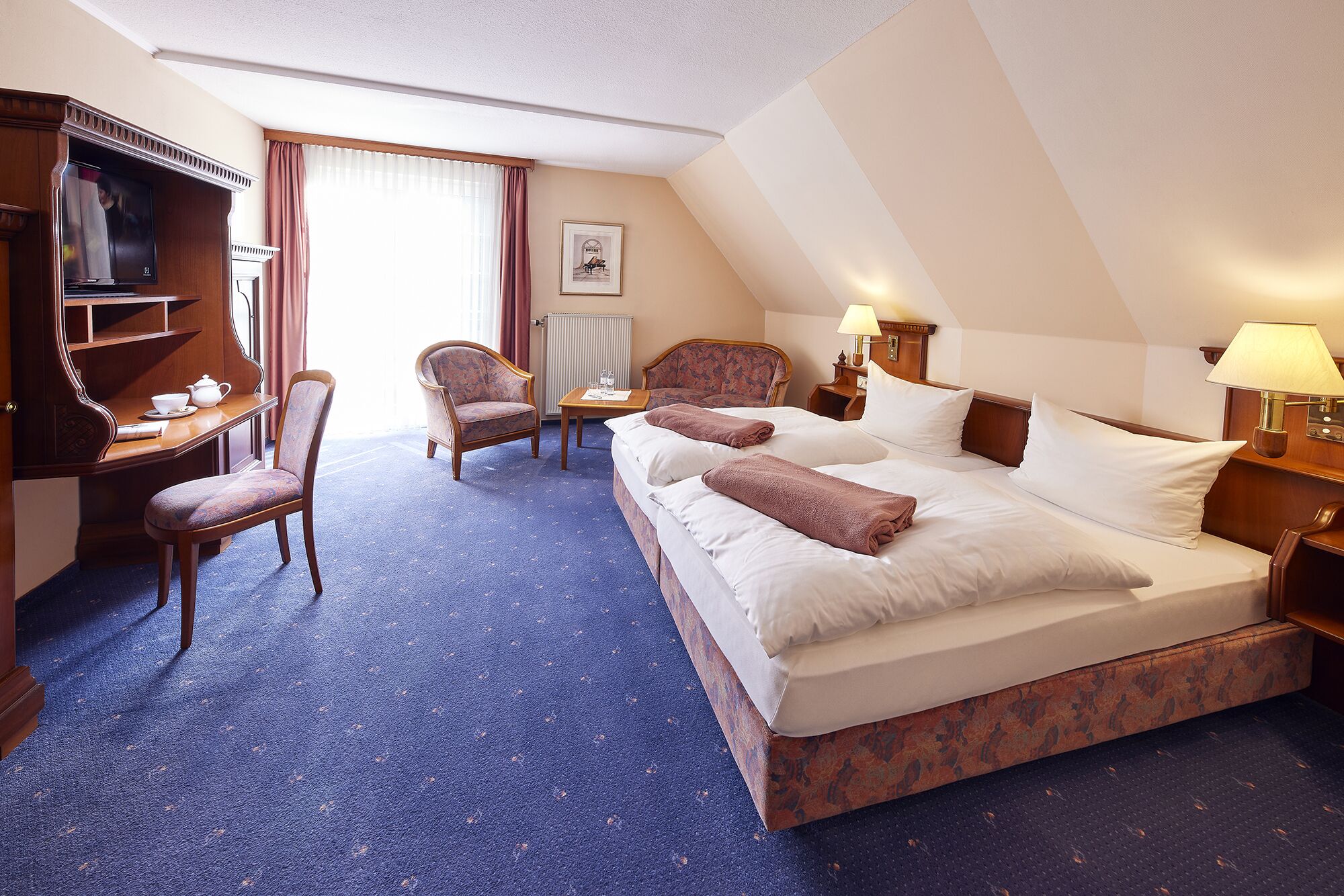 A hotel room with a large bed, a desk, a chair, and a television.