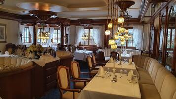 Un comedor formal con una larga mesa dispuesta para una comida, sillas de madera y una araña.
