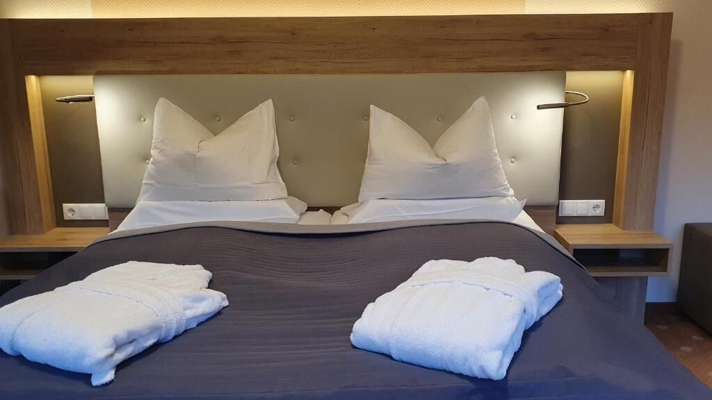 Un lit bien fait, avec du linge de lit blanc et des oreillers, une tête de lit en bois et des tables de chevet avec des lampes.