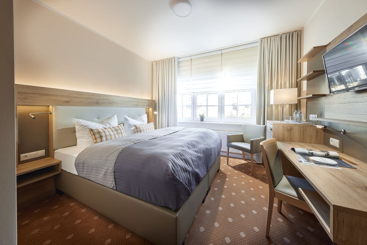 A hotel room with a bed, desk, chair, TV, and window with curtains.
