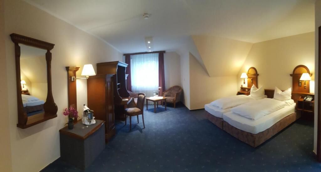 Ein Hotelzimmer mit Bett, Schreibtisch, Stuhl, Fernseher und einem Vorhangfenster.