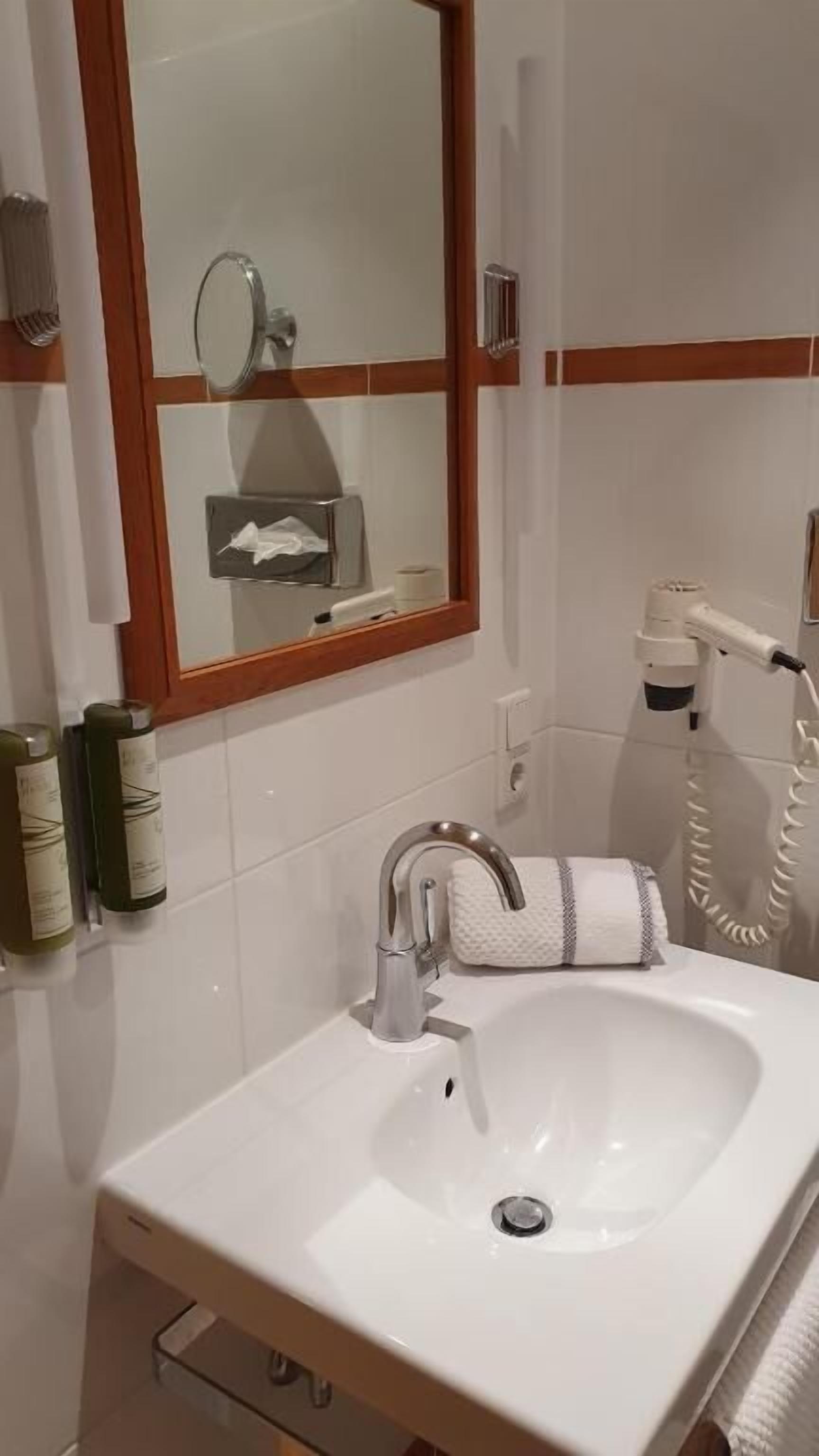 Un baño con lavamanos blanco, un espejo, una toalla y un secador de pelo.