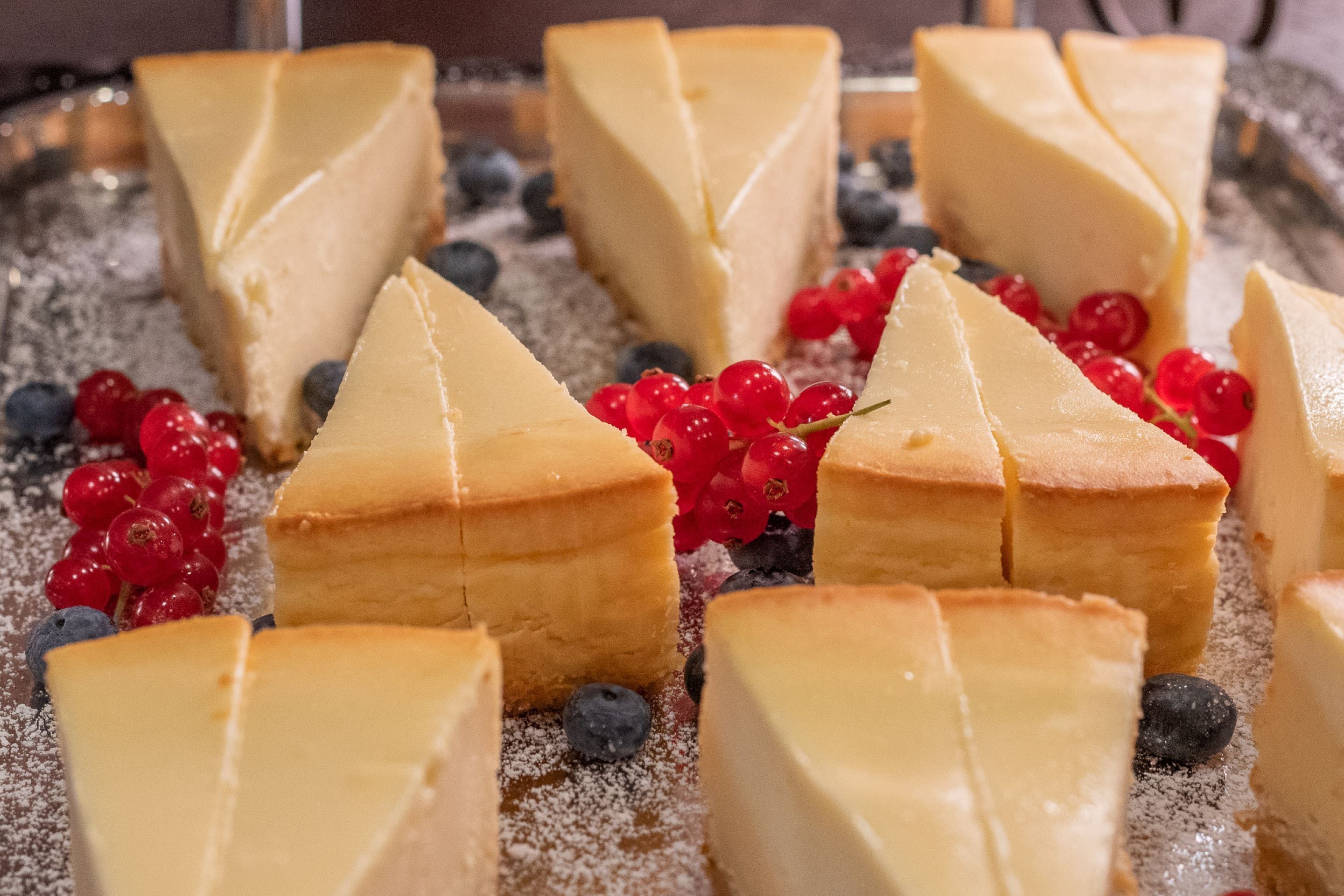 Una bandeja de postres con porciones triangulares de pastel de queso y arándanos.