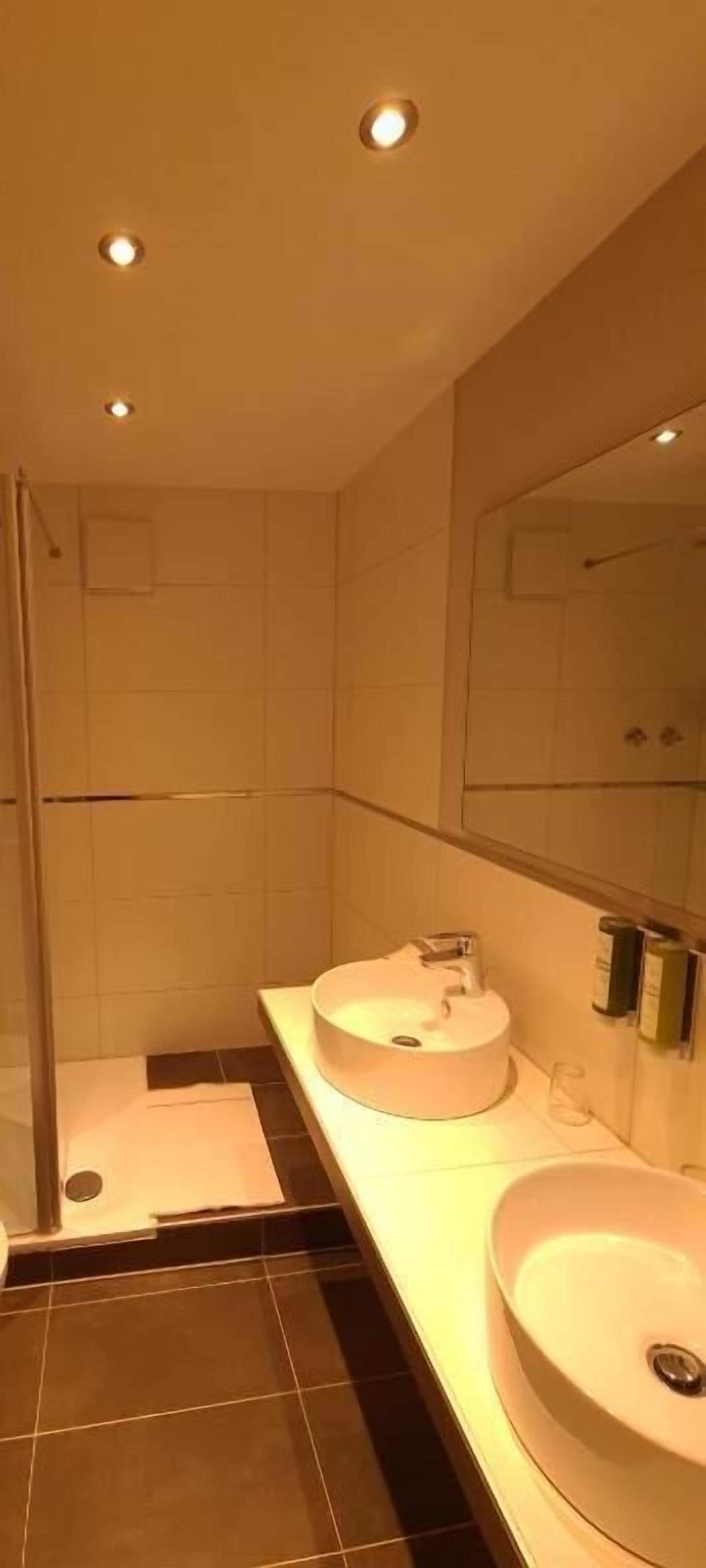 A modern bathroom with two sinks, a shower, and a large mirror.