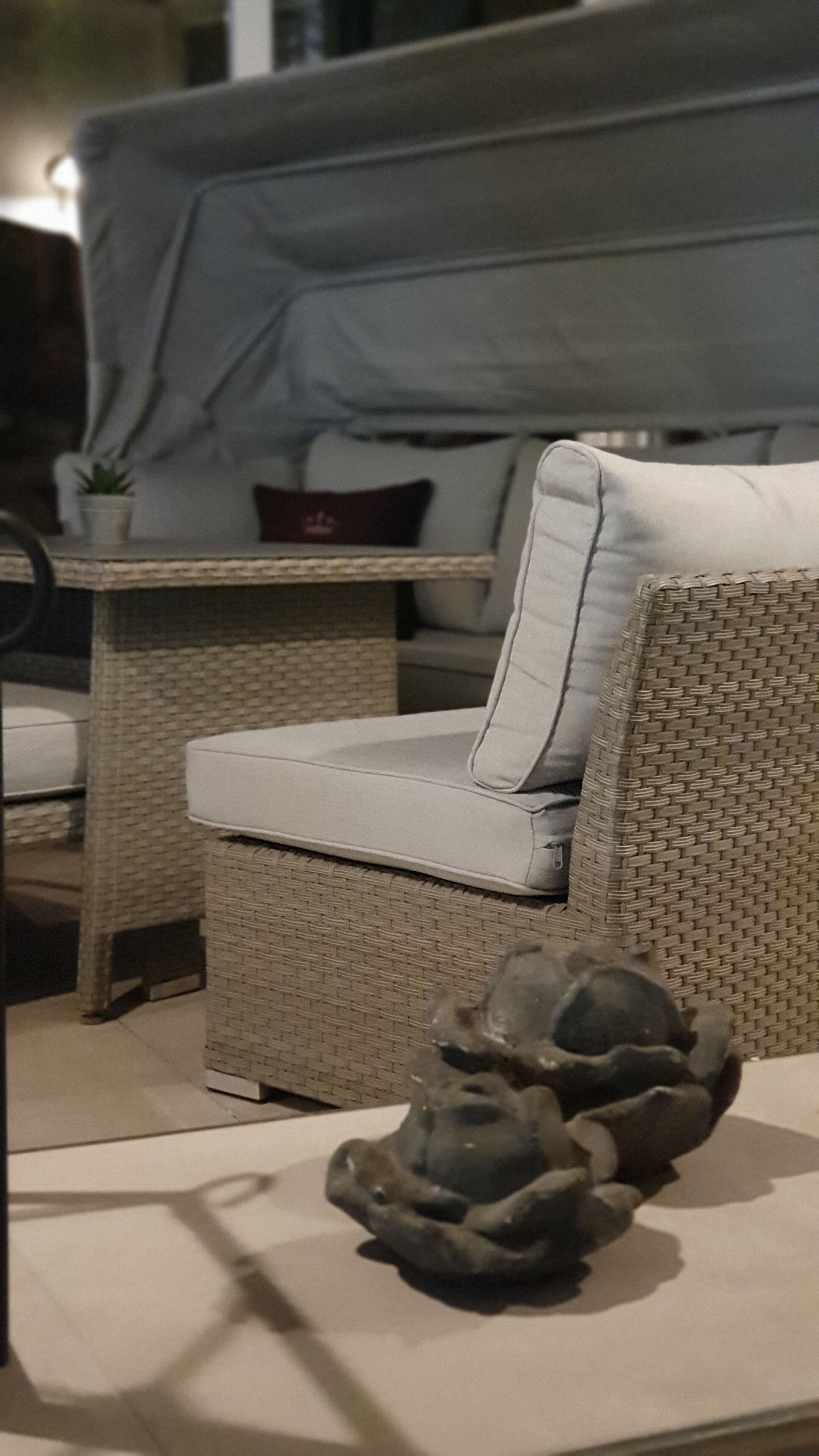 A wicker sofa with a cushion, a small table with a plant, and a decorative stone arrangement.