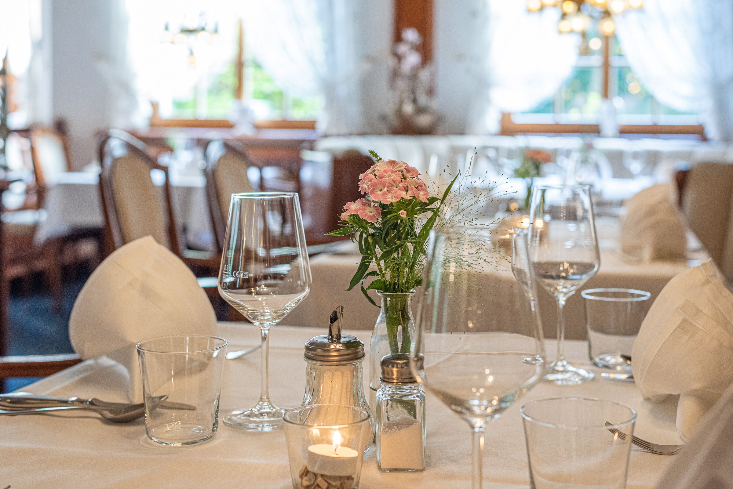 A dining table set with wine glasses, a candle, salt and pepper shakers, and a vase with flowers.
