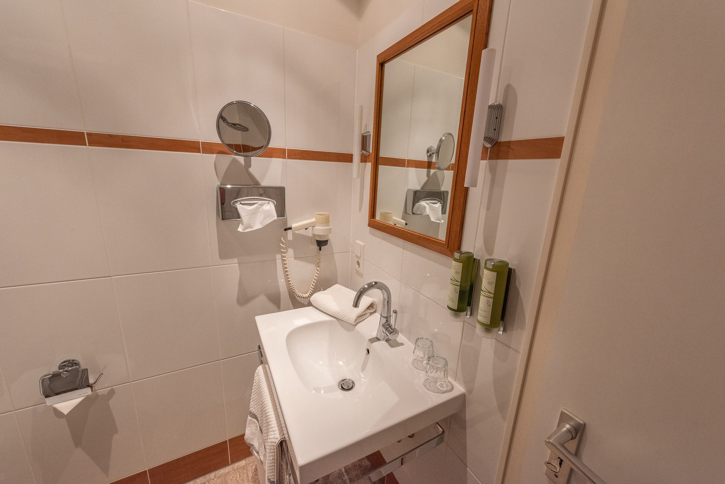 A bathroom with a white sink, a mirror, and toiletries on the wall.