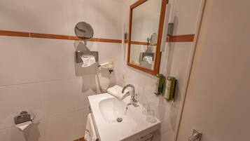 A bathroom with a white sink, a mirror, and toiletries on the wall.