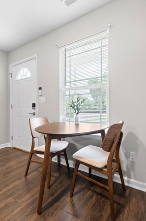 A dining area with a round table, two wooden chairs, a potted plant, and a window with blinds. - Jan Dates Open: Pet friendly near 3 hospitals (Chattanooga)