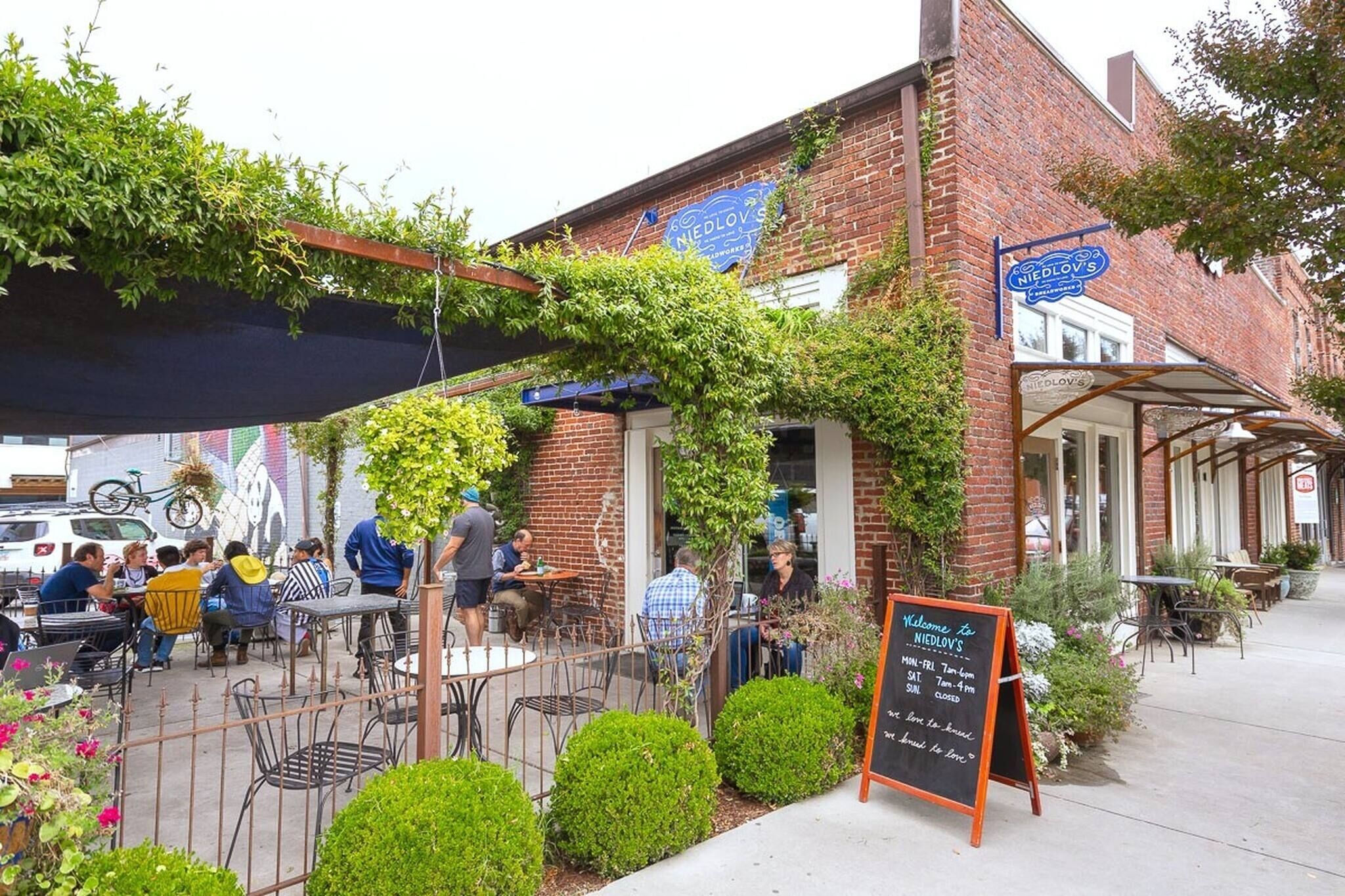 Ein Straßencafé mit Tischen und Stühlen, ein Backsteinhaus und ein Schild.