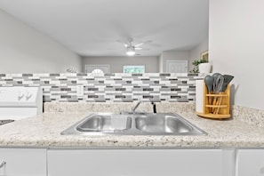 A kitchen with a granite countertop, stainless steel sink, and a backsplash with gray and white tiles. - Jan Dates Open: Pet friendly near 3 hospitals (Chattanooga)