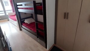 Quarto com beliches, um guarda-roupa e porta para uma varanda.