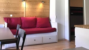 Um espaço de estar moderno com parede de madeira, um sofá vermelho, um armário branco e uma área de jantar com mesa e cadeiras.