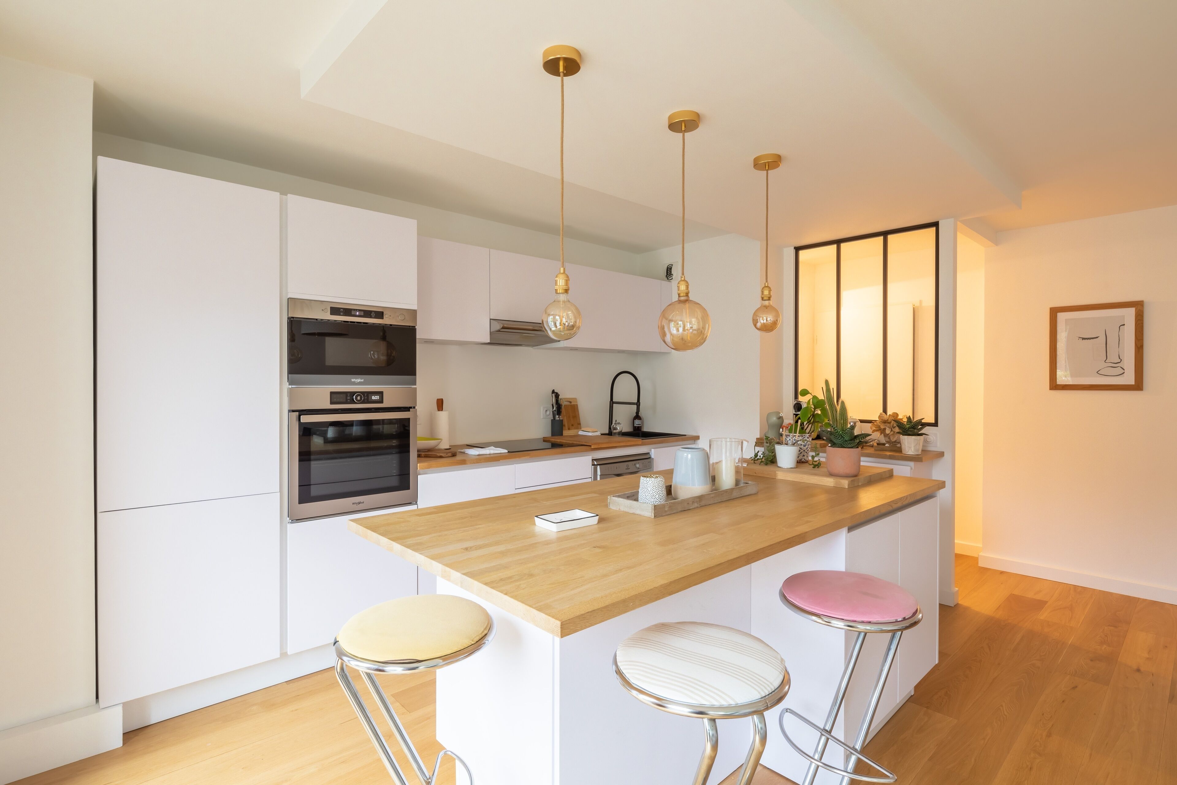 Una cocina moderna con armarios blancos, una isla de madera, electrodomésticos de acero inoxidable e iluminación colgante.