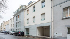 Une rangée de voitures garées le long d’une rue, avec un immeuble doté de nombreuses fenêtres et une entrée de garage.