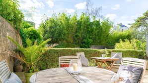 Une terrasse extérieure avec une table ronde en bois, deux chaises et un coussin.