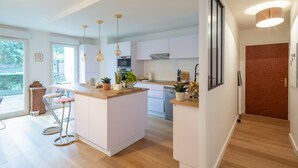 Une cuisine moderne dotée d’un îlot central, de luminaires suspendus et offrant une vue sur l’extérieur.