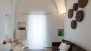 A modern living room with a brown sofa, a staircase leading to a balcony, and a wall-mounted shelf with decorative items. - Terrazza Primavera by Wonderful Italy (Ostuni)