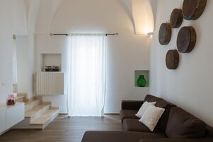 Una sala de estar moderna con un sofá marrón, una escalera que conduce a un balcón y un estante montado en la pared con objetos decorativos.