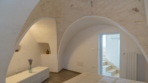 A bedroom with a large bed, a vanity with a vase, and a staircase leading to an upper floor. - Terrazza Primavera by Wonderful Italy (Ostuni)