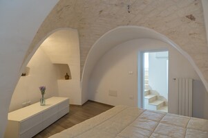 Un dormitorio con una cama grande, un tocador con un florero y una escalera que conduce a un piso superior.