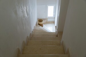 Una escalera que lleva a una habitación con ventana, puerta y un bote de basura.