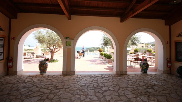 A covered outdoor area with stone flooring, three arched openings, and potted plants.