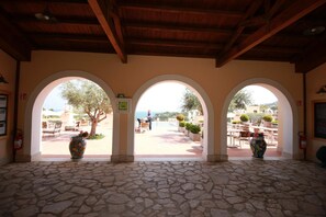 A covered outdoor area with stone flooring, three arched openings, and potted plants.