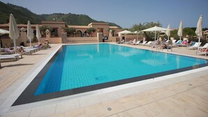 A rectangular swimming pool with a tiled deck, surrounded by lounge chairs and umbrellas.