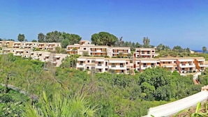 A hillside residential area with terraced houses, lush greenery, and a clear view of the sea.