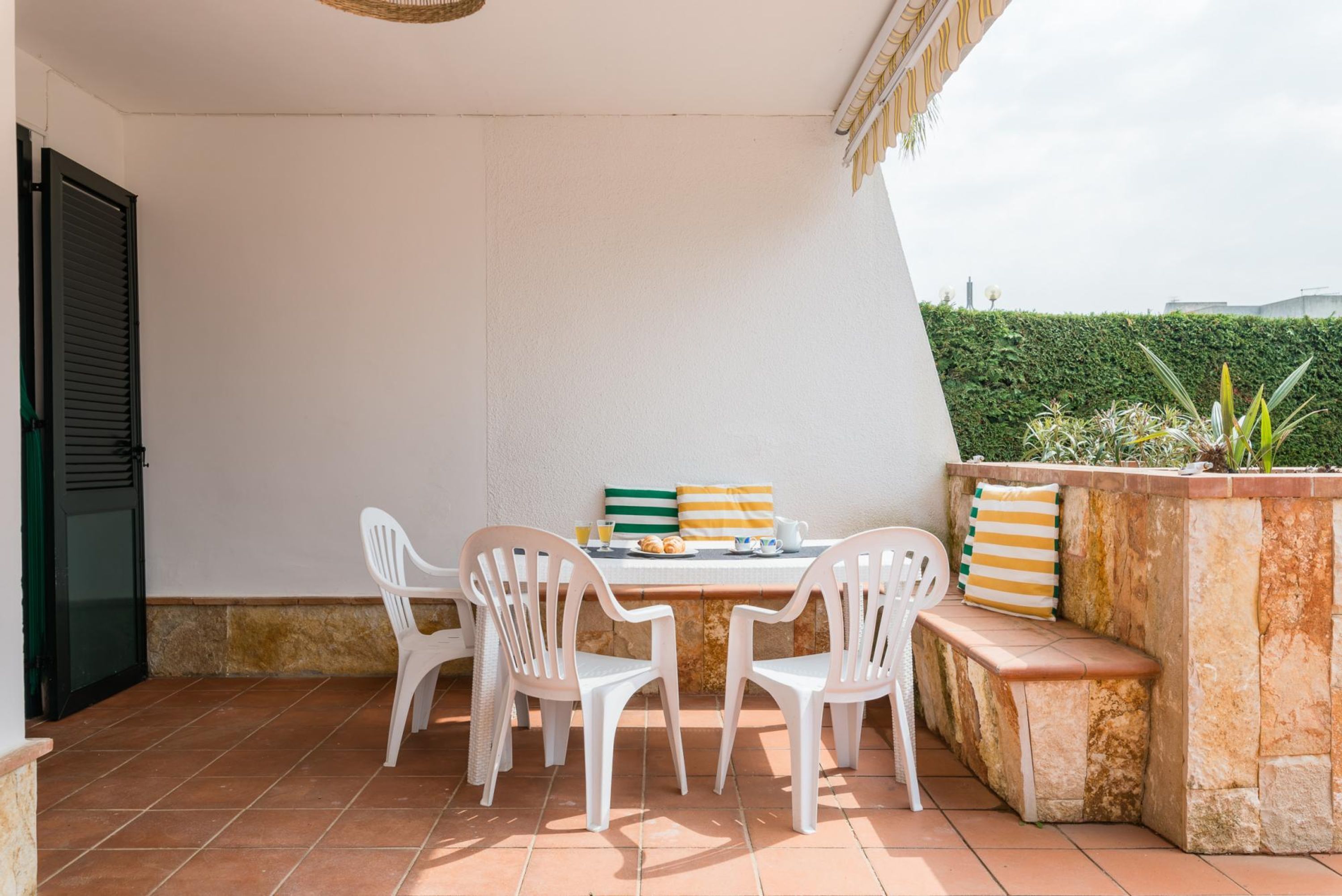 A patio with a table and chairs, a bench, and a stone planter with plants.