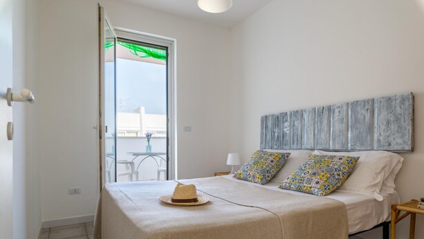 Camera da letto con un letto, due cuscini, un comodino, un'opera d'arte appesa al muro e vista attraverso una porta aperta.