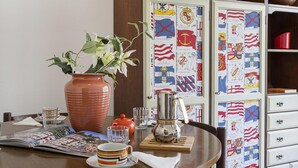 Ett matbord med en vas med blommor, en kaffekanna och en tidning.