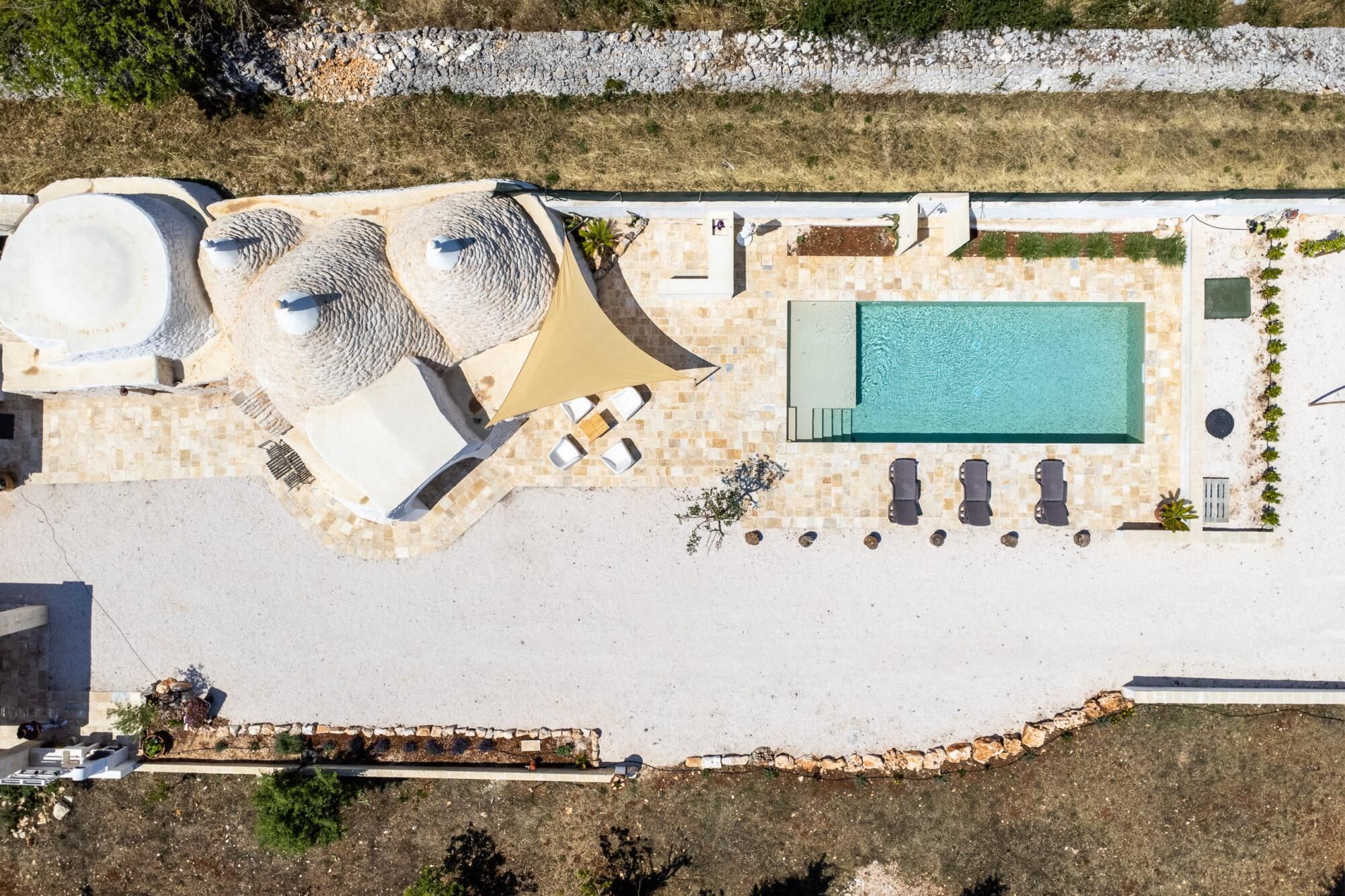 Vista aérea de un resort con piscina, tumbonas, jacuzzi y una zona de estar cubierta.