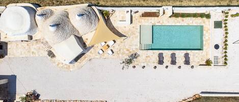 Vista aérea de un resort con piscina, tumbonas, jacuzzi y una zona de estar cubierta.