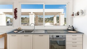 A modern kitchen with a large window, built-in oven, and white cabinetry. - Trullo La Dolina con Piscina by Wonderful Italy (Ostuni)