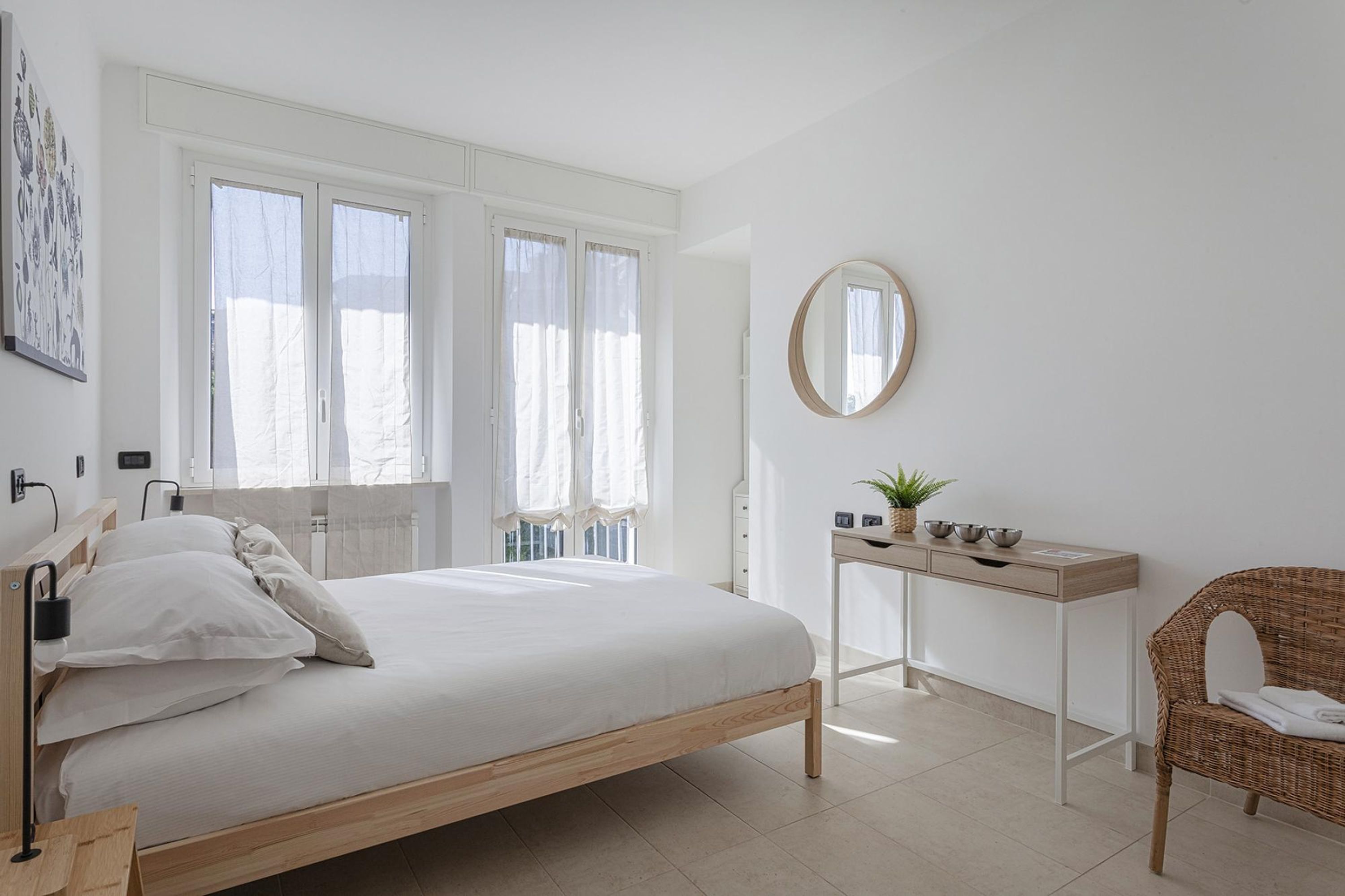 Une chambre à coucher avec un lit, une table de chevet dotée d’un miroir, un fauteuil en osier et une fenêtre avec des rideaux.