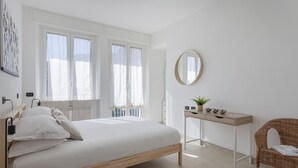 Une chambre à coucher avec un lit, une table de chevet dotée d’un miroir, un fauteuil en osier et une fenêtre avec des rideaux.