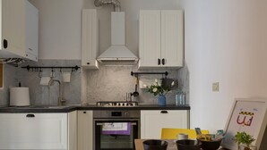 A modern kitchen with white cabinets, a stainless steel range hood, an oven, and a countertop with a sink.
