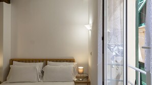 A bedroom with a wooden headboard, a bedside table with a lamp, and a window with a view of a balcony.