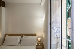 Ein Schlafzimmer mit einem Holzkopfteil, einem Nachttisch mit Lampe und einem Fenster mit Blick auf einen Balkon.