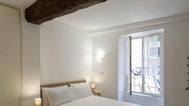 A bedroom with a wooden bed, two bedside lamps, a window with a view, and a wall-mounted light fixture.